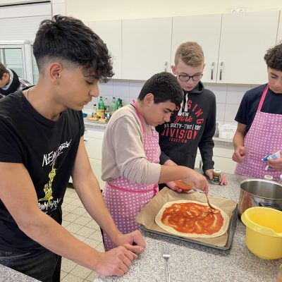 Unter kritischer Begutachtung seiner Mitschüler bestreicht Poyraz die XXL-Pizza mit Tomatensauce.